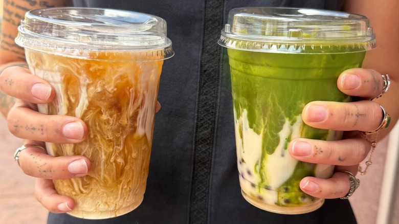 Two hands holding a cold brew and an iced matcha in to-go cups from Paramount Cafe