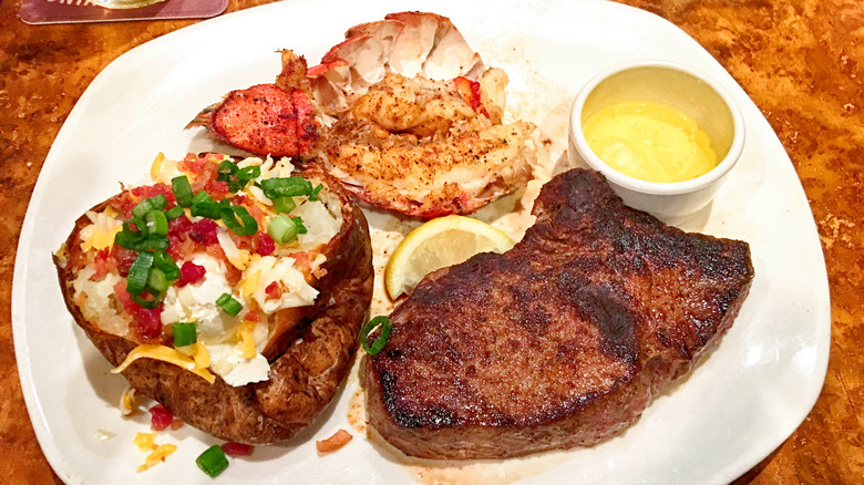 Steak, loaded baked potato, and lobster tail on white plate