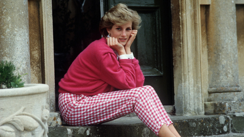 Princess Diana sitting on the steps with her face in her hands while smiling