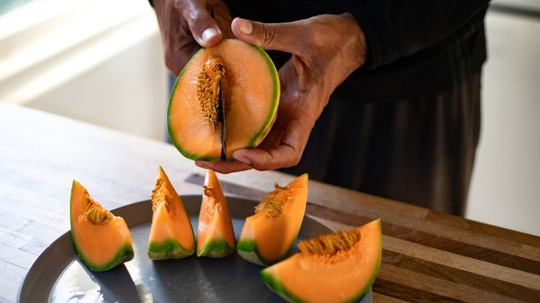 A hand cuts cantaloupe into weddges