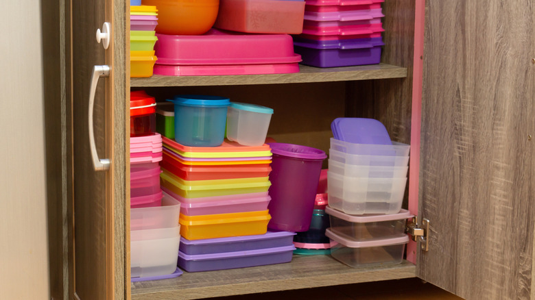 An open cupboard full of colorful plastic food storage containers.
