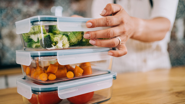 A person storing vegetables in plastic tubs.