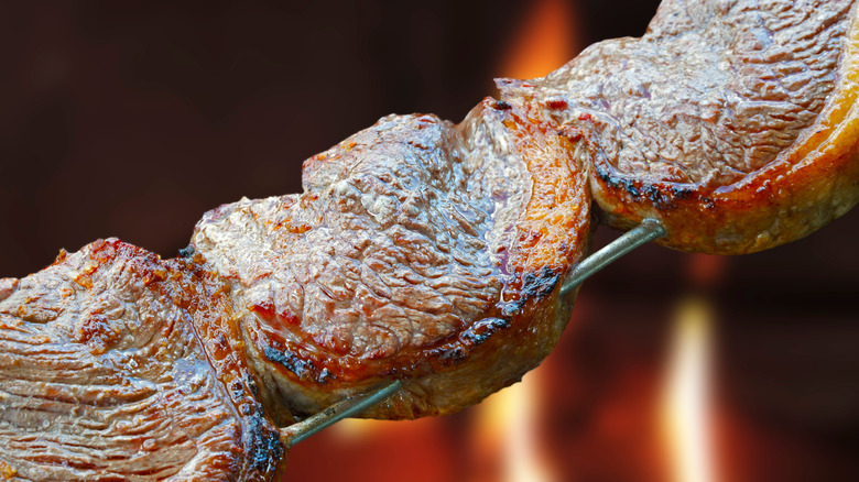 Three pieces of cooked meat on a metal skewer, with flames
