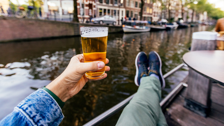 A person holding a glass of beer in their hand in front of a river.