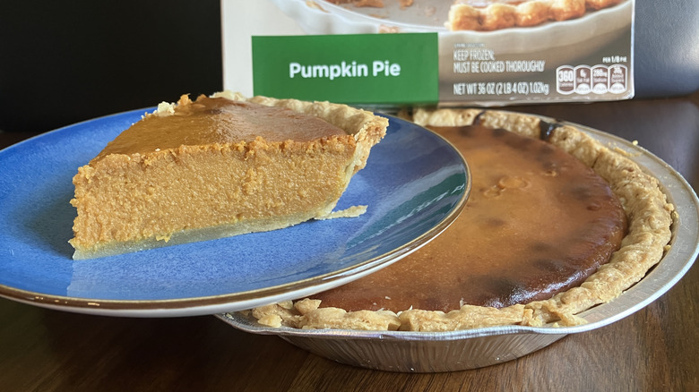 Slice of pumpkin pie on plate balanced on top of remainder of pie.