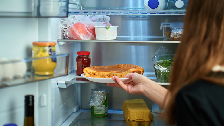 Woman placing pie on a plate into a fridge