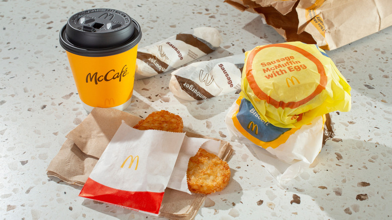 Various McDonald's breakfast items on counter including hash browns, McMuffins, coffee, and burritos.