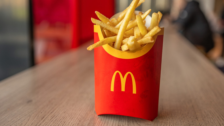 A cardboard tub of McDonalds fries stood upright on a table.