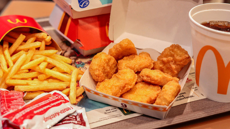 A McDonalds order of chicken nuggets with fries, a drink, and sauce sachets sitting on a table.