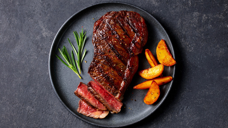 Beef steak with roasted potato wedges and rosemary served on a black plate