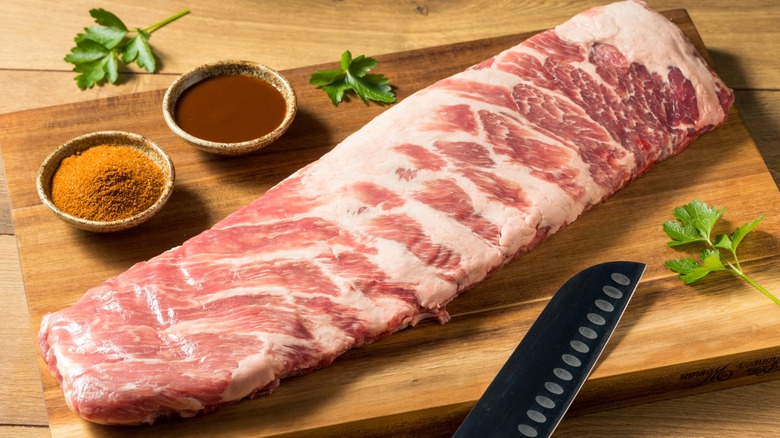 Raw St. Louis-style spareribs on wood board with seasonings and knife on the side