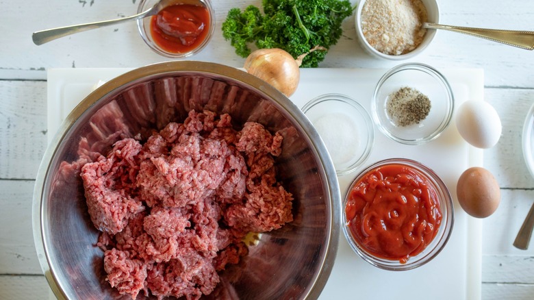 Top down view of ingredients for making meatloaf, including ground meat in a bowl and bowls of sauce