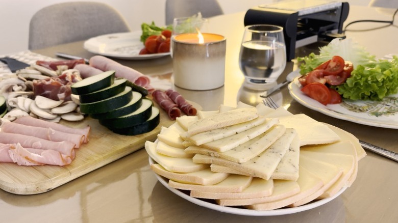 Sliced Raclette cheese on a plate with fresh vegetables and cured meats