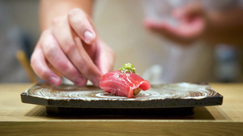 A sushi chef delicately placing a piece of tuna nigiri on a ceramic plate at an omakase-style Japanese restaurant
