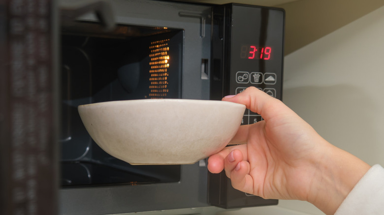 A person putting a white bowl into a microwave oven.