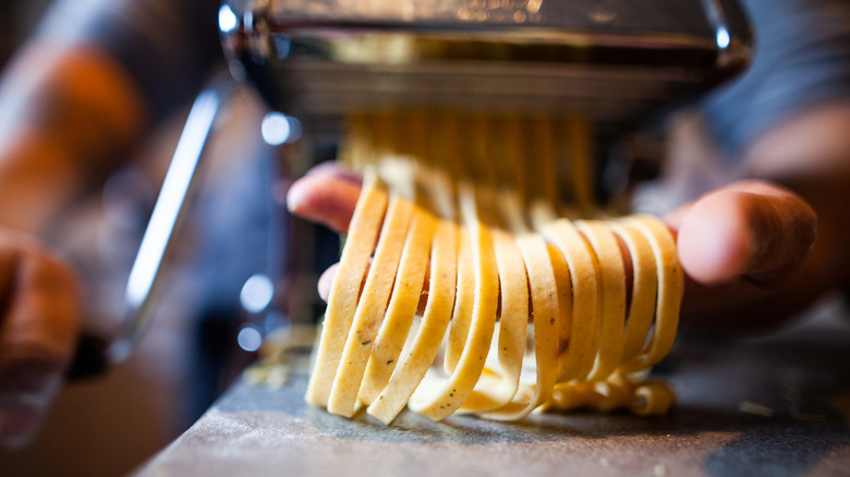 A person cranking homemade pasta dough through a pasta machine