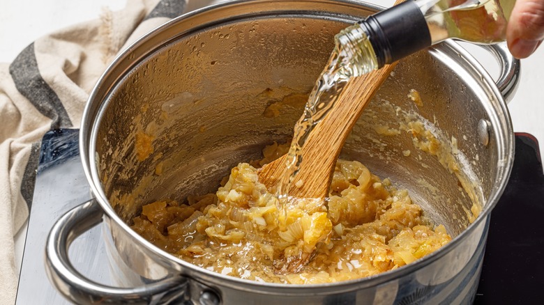 hand pours white wine to deglaze pan
