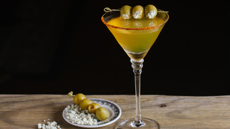 Skewered blue cheese olives suspended above a martini