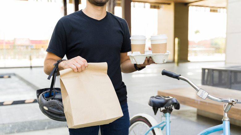 Food delivery worker with bicycle holding paper bag and coffee