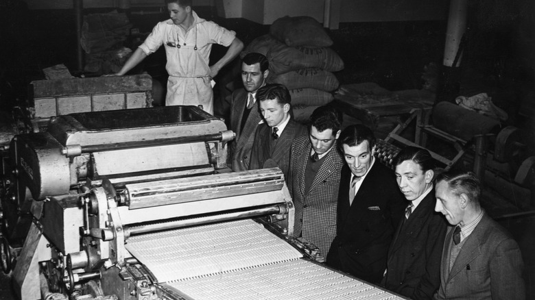 Vintage photo of men watching candy biscuits being rolled out on a factory machine conveyor belt