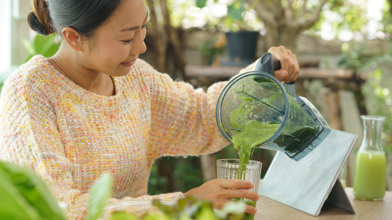 Woman pouring a green smoothie from a blender into a glass