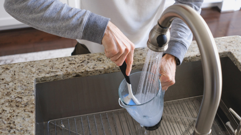 Hands cleaning a blender jar under running water
