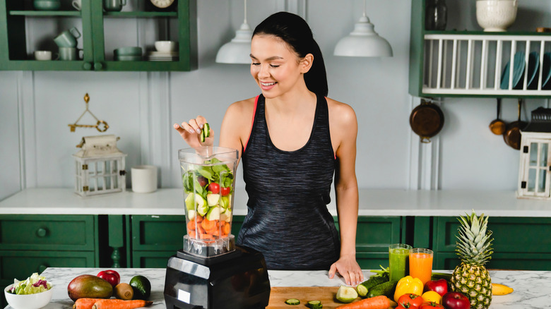 Woman filling a blender with fruits and vegetables