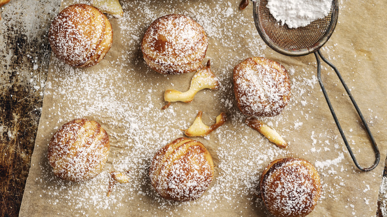 Pastries sit on parchment paper with a dusting of icing sugar.