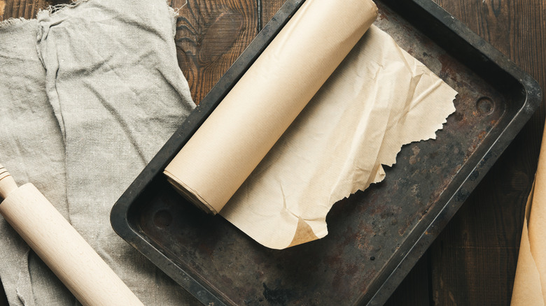 A roll of parchment paper sits on a baking pan. A rolling pin and cloth sit in the background.