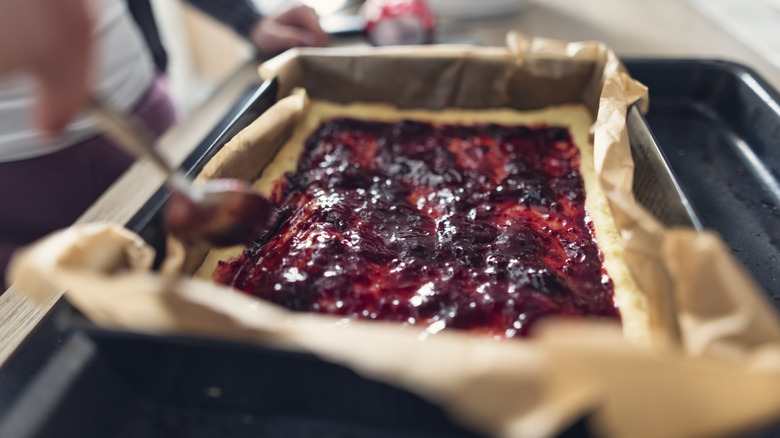 A tart rests on a bed of parchment paper inside of a baking pan. A spoon is filling the tart.