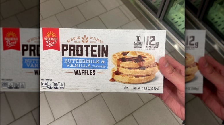 Close up of customer holding a box of Breakfast Best brand Buttermilk & Vanilla protein waffles in Aldi frozen foods aisle.