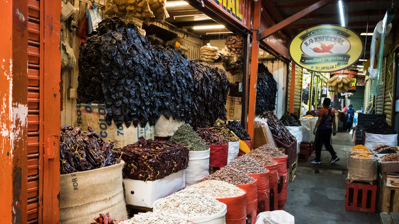 A Oaxacan marketplace with dried peppers, nuts, and grains in large baskets or hanging