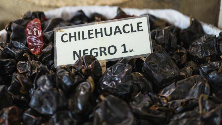 Dried chilhuacle negro peppers in a basket at a market, labeled with a white sign