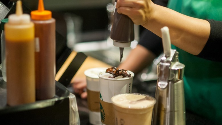 Barista adds whipped cream and sauce to a drink order.