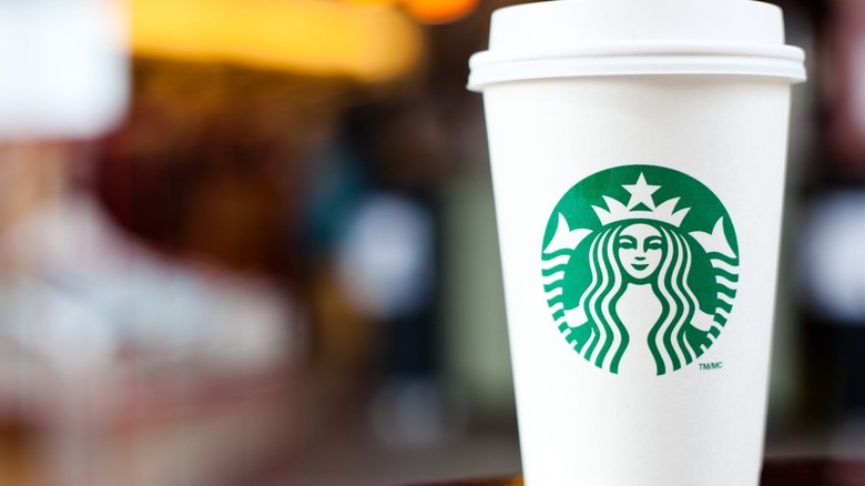 Iconic white Starbucks coffee cup sits on table with a blurred background.
