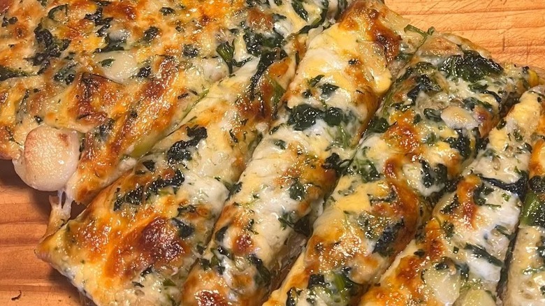 A close-up of cheesy flatbread topped with spinach.