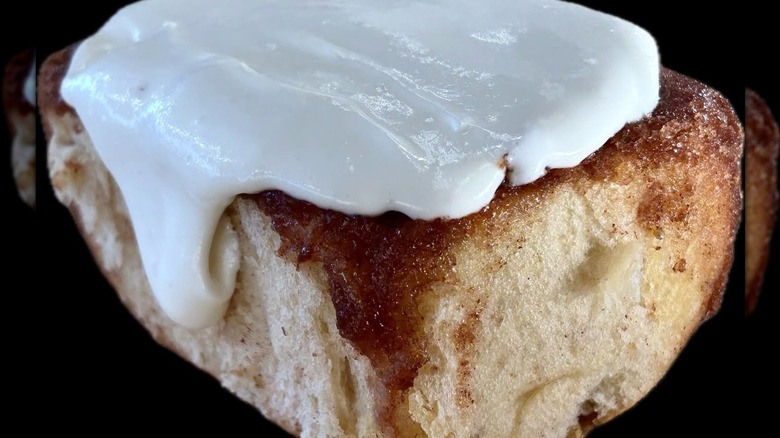 A close-up of a large freshly baked cinnamon rolls, glistening with cream cheese frosting.
