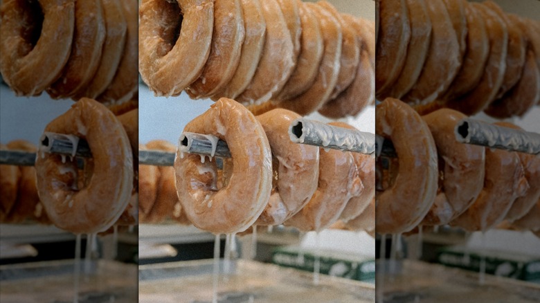 Rings of freshly made Peachey's donuts drip excess glaze as they hang in rows.