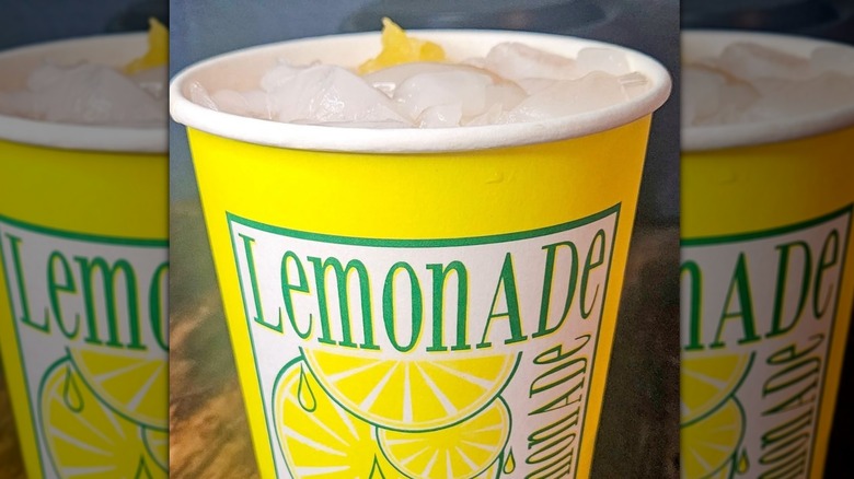 A yellow cup of lemonade shake up filled to the top with ice and lemon pieces.