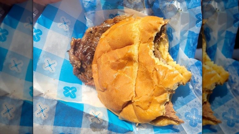 A grilled ribeye sandwich, with the steak hanging out of the soft bun.