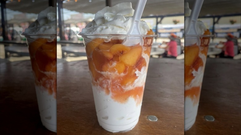 A clear cup of vanilla ice cream, freshly cut peaches, and whipped cream.