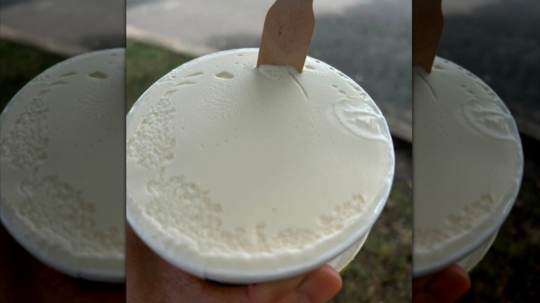A carton of Ollie B's peach flavored honey ice cream, with a wooden spoon sticking out of the top.