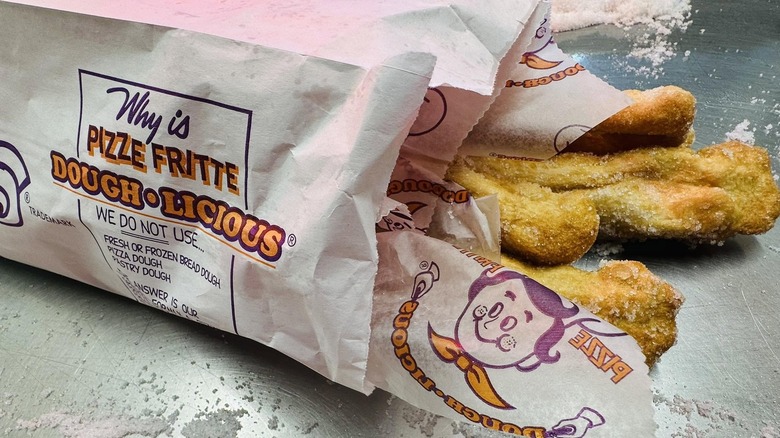 A Bag of Villa Pizze Fritte fried dough covered in sugar with extra sugar on the counter.