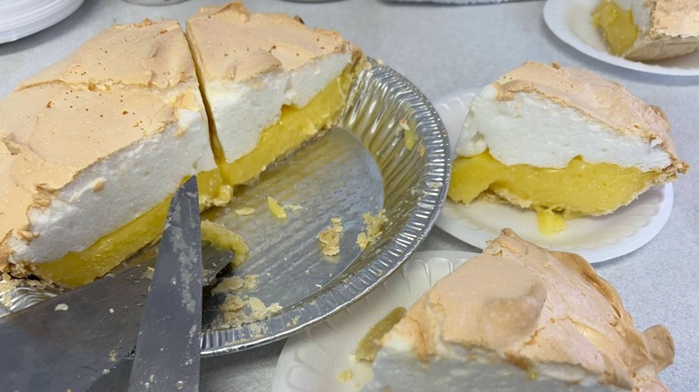 Slices of lemon meringue pie in pie tin and on plates.