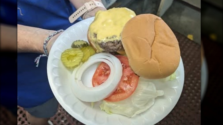 A Douglas Rotary Club cheeseburger with pickles, onions, tomatoes, and lettuce on a styrofoam plate.