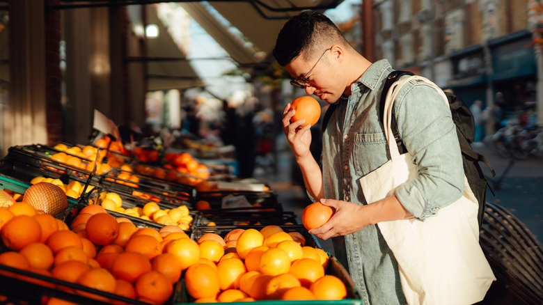 Young man smells oranges outside fruit market