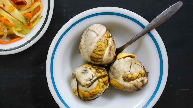 Ready to eat fertilized duck eggs on white bowl served with the pickled mixture of carrot, mango, papaya and ginger.