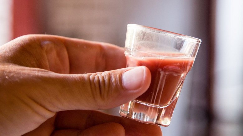A shot glass of cobra blood held by a hand in closeup
