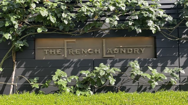 A dark brown outdoor wall with a lighter brown inset sign that reads "The French Laundry" surrounded by lush vines