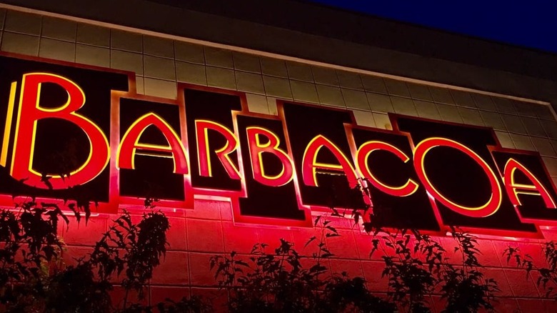Exterior of Barbacoa restaurant lit at night; "Barbacoa" is spelled out in red capital letters in red outlined in yellow on black squares